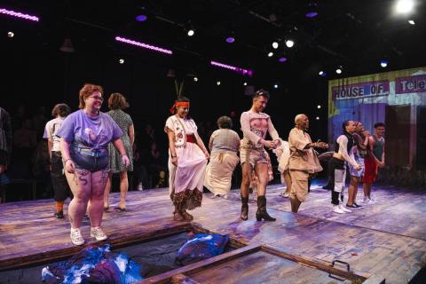 Performers stand on stage in a line jumping. In the background, the backdrop reads House of Telescopes.